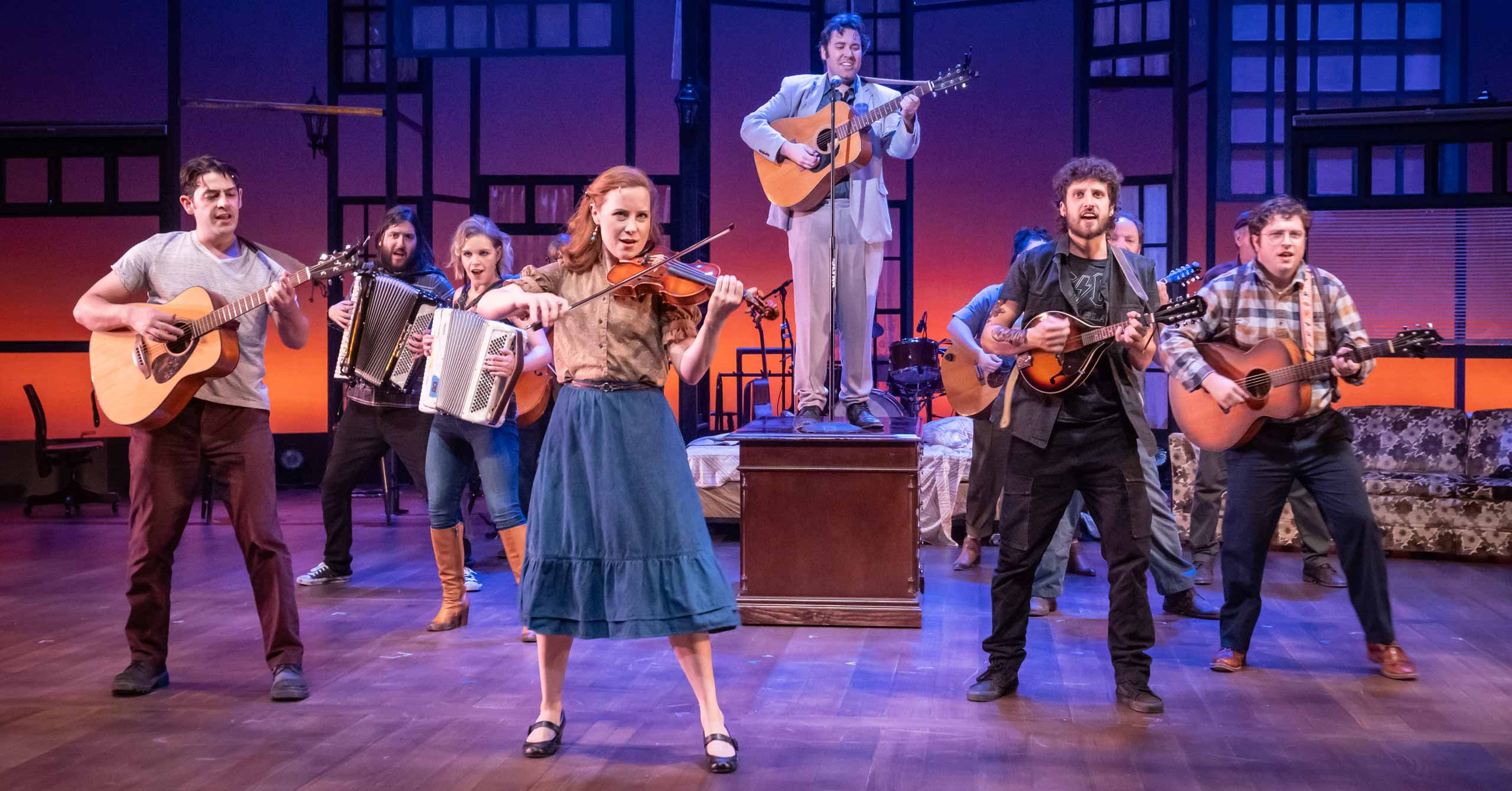 A group of folk musicians holding instruments perform onstage
